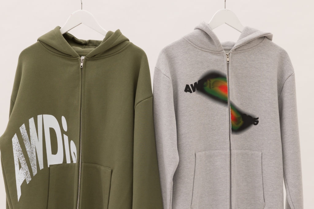 Two zip-up hoodies on hangers: one in olive green with bold white branding and the other in grey with a colourful printed design.