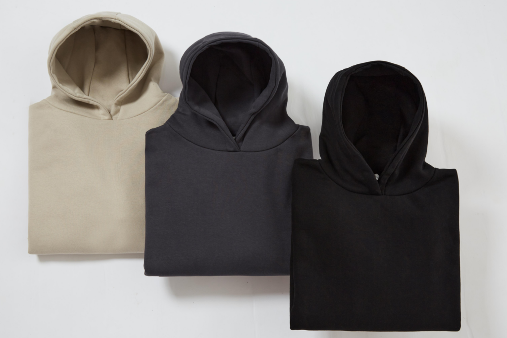 Three folded hoodies in sand, charcoal, and black on a white background.