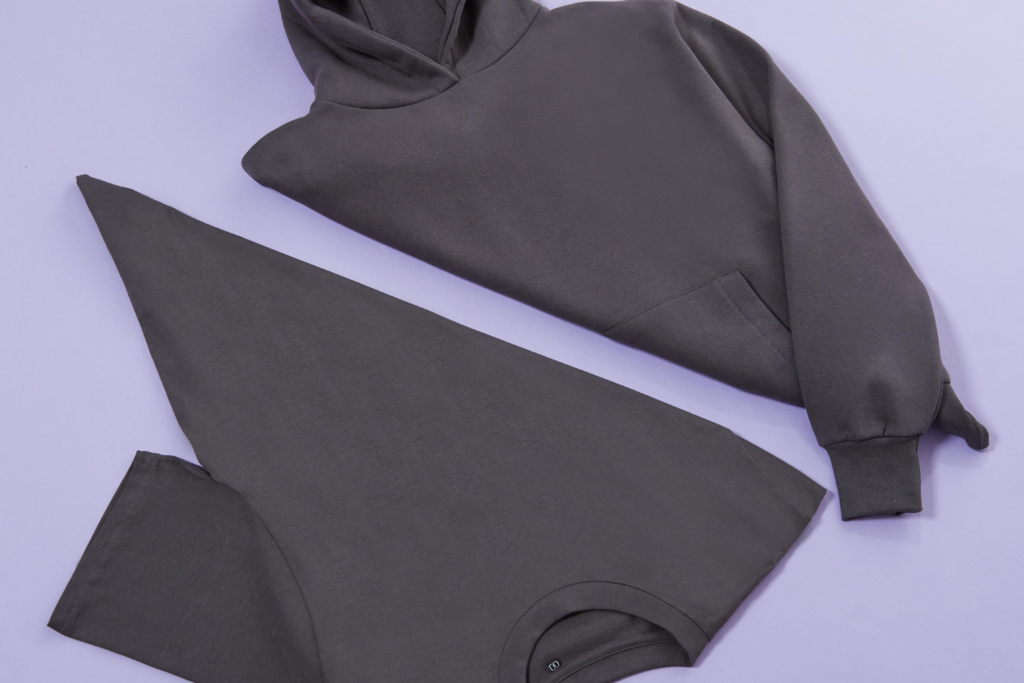 Charcoal grey hoodie and t-shirt folded on a lilac background.